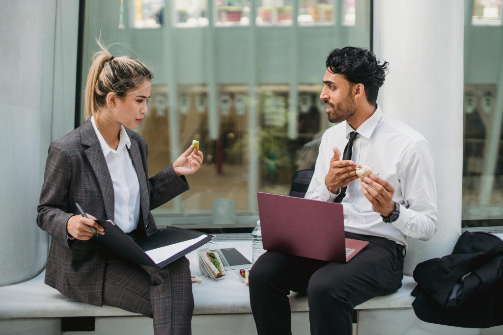 Two professionals discussing work during a casual lunch break indoors.